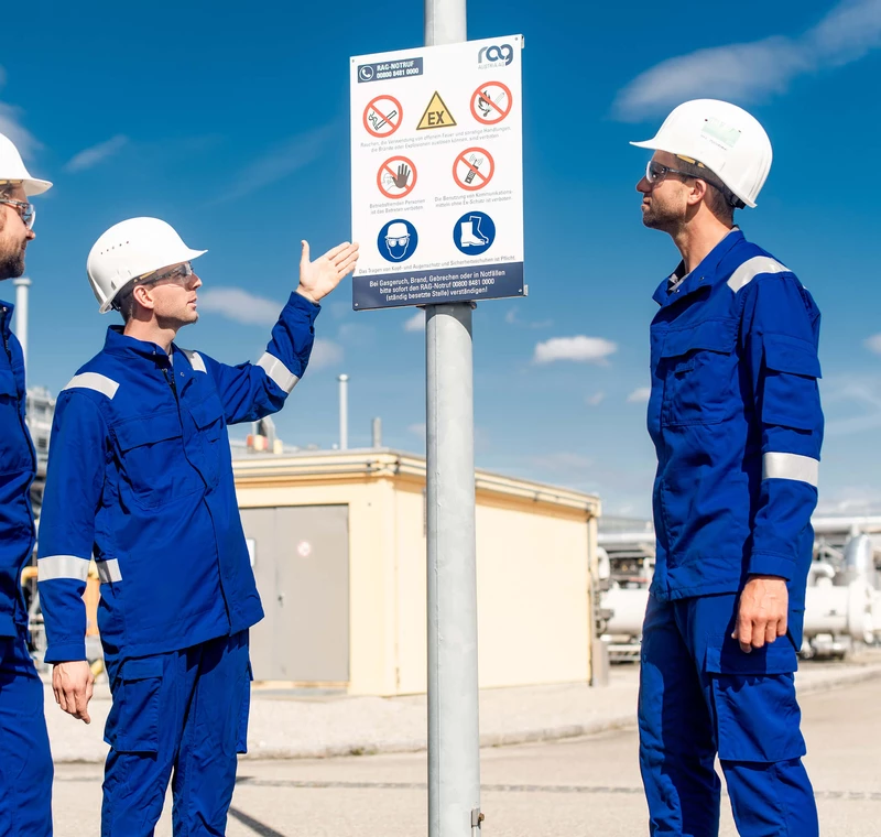 RAG Mitarbeiter mit Schutzkleidung deuten auf ein Hinweisschild