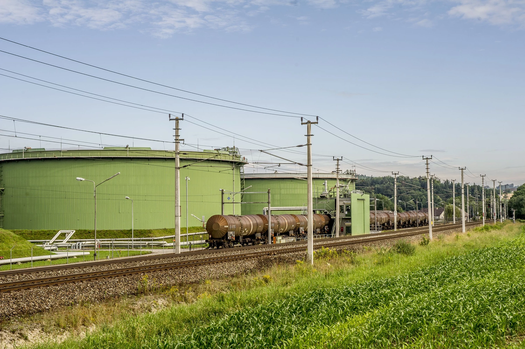 Tanks hinter Bahngleisen und grüner Wiese